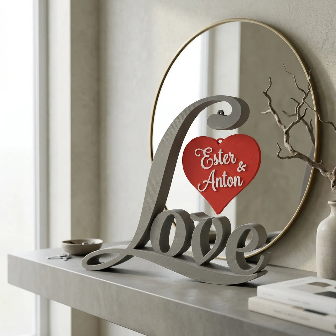 Pieza tipográfica Love en gris mate con corazón rojo personalizado suspendido y nombres Ester y Anton en relieve blanco.