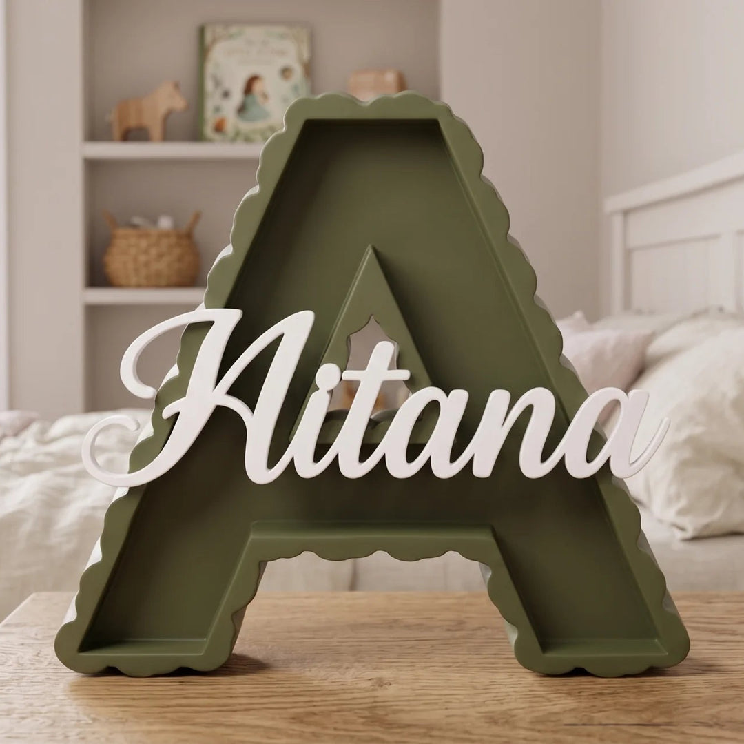 Letra A en verde oliva con el nombre Aitana sobre una mesa junto a la cama en una habitación infantil