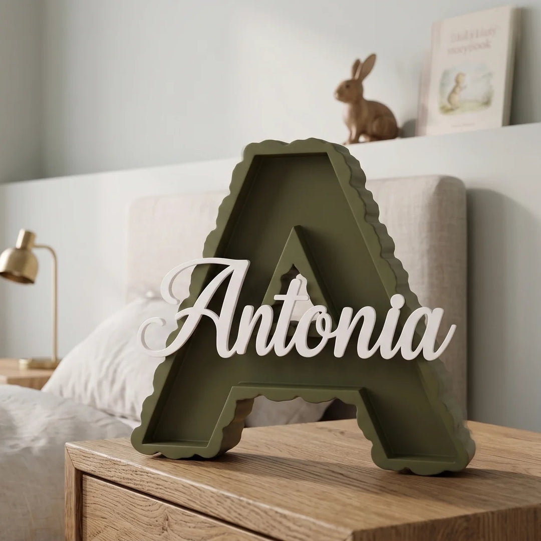 Letra A en verde oliva con el nombre Antonia sobre una mesilla junto a la cama de un dormitorio infantil