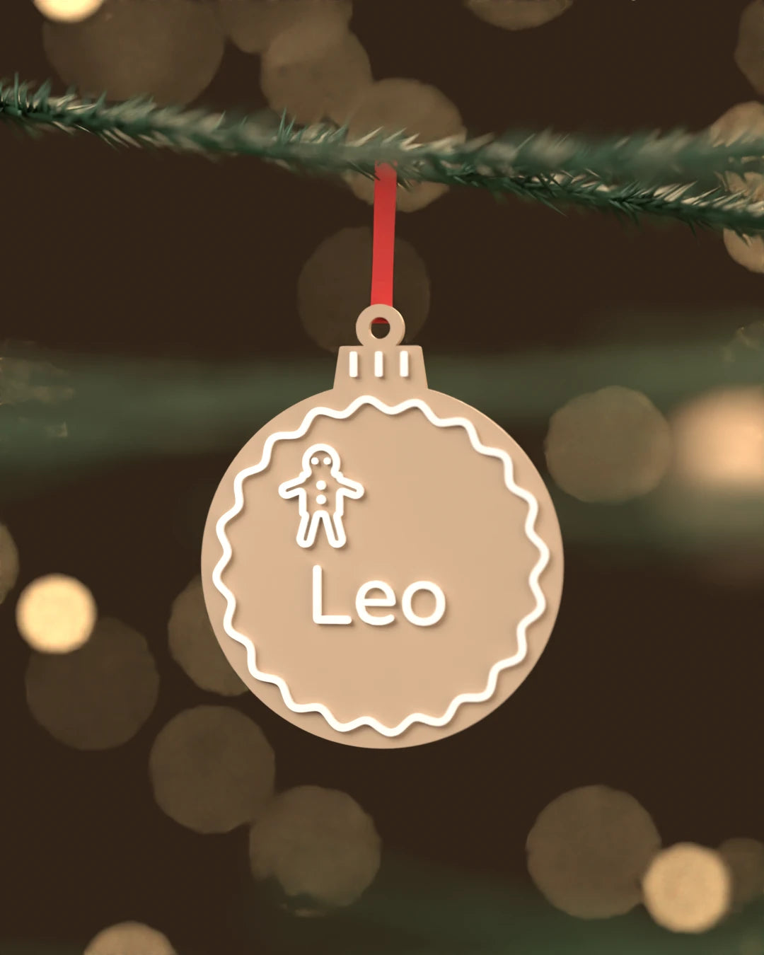 Bola de Navidad Jengibre color marrón latte con glaseado blanco y el nombre Leo, colgada de una rama de abeto