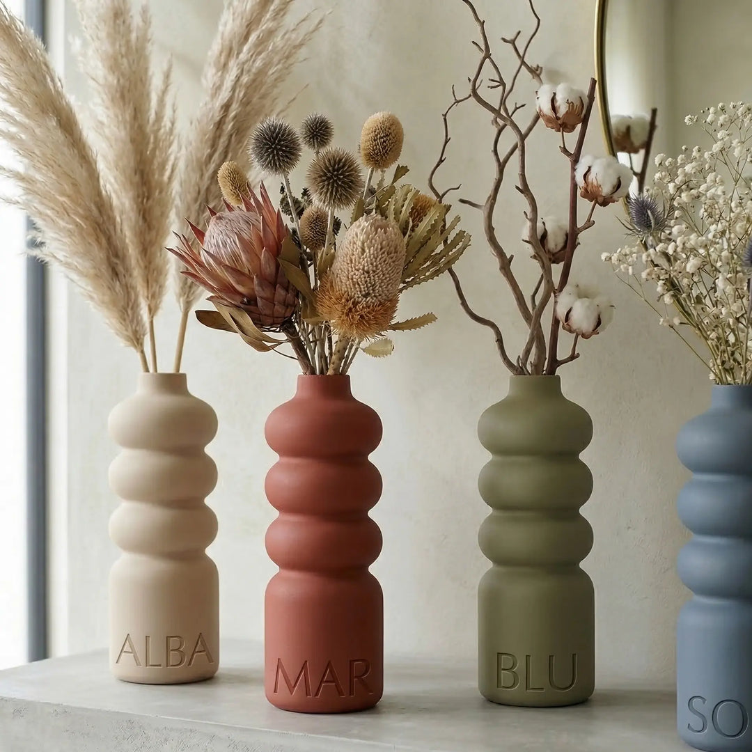 Jarrón de diseño sinuoso beige con nombre ALBA en relieve en la base, estilo minimalista orgánico.