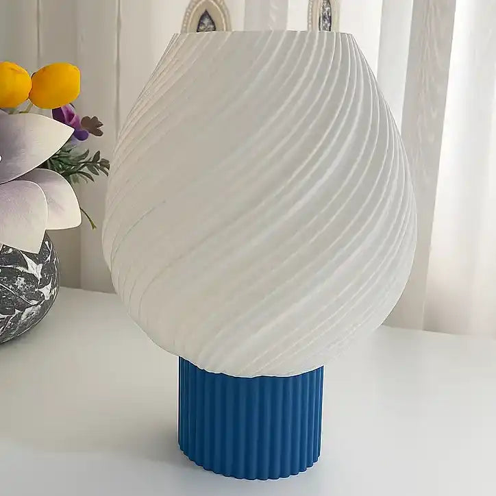 Lámpara de mesa moderna con pantalla blanca en espiral y base cilíndrica azul texturizada sobre superficie blanca. Base Personalizable