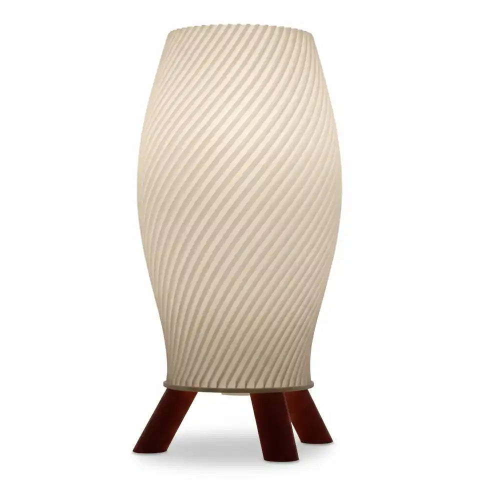 Lámpara de mesa de diseño helicoidal en color crema con base trípode de patas oscuras efecto madera sobre superficie blanca.