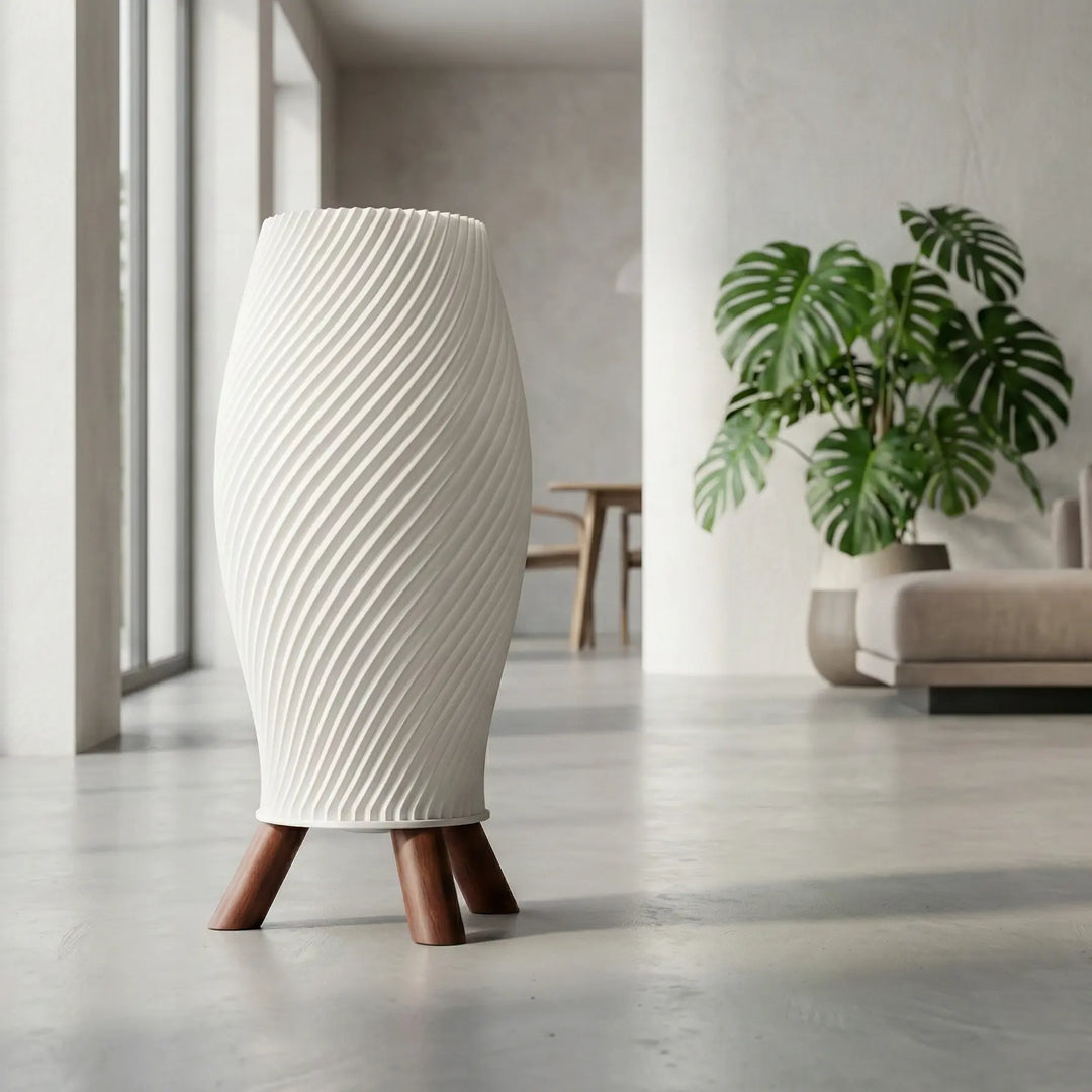 Lámpara de mesa de diseño helicoidal en color crema con base trípode de patas oscuras efecto madera sobre superficie blanca.