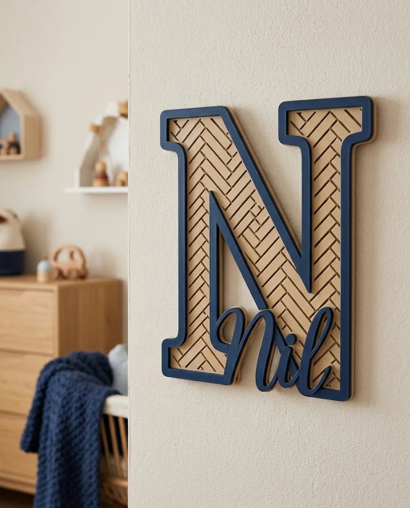 Letra N con el nombre Nil, patrón calado en espiga arena del desierto y marco azul oscuro, colgada en una habitación infantil escandinava junto a una cómoda de roble