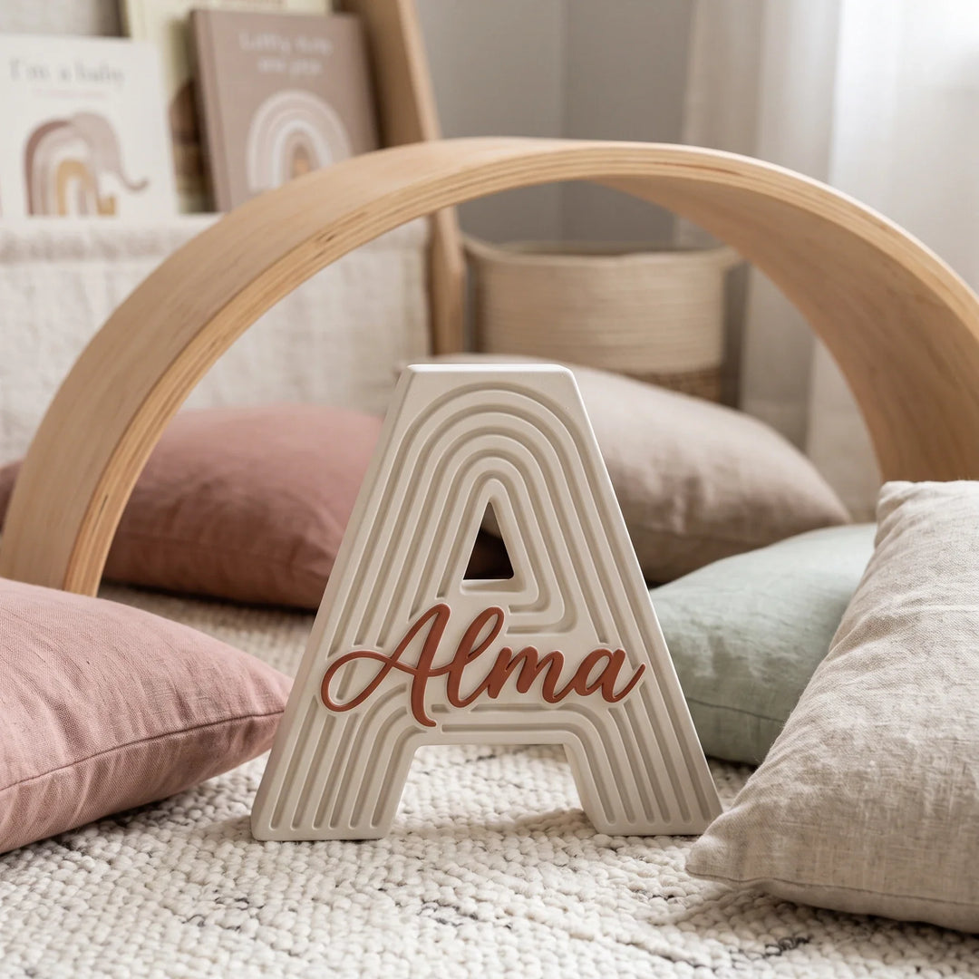 Letra A personalizada Arcoíris en un rincón de juego con cojines y arco de madera
