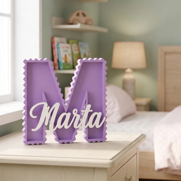Letra M en zig zag lila con el nombre Marta sobre una mesilla en una habitación infantil