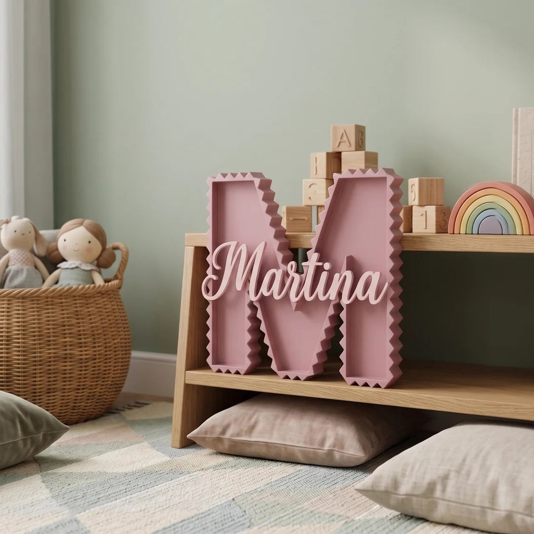 Letra M en zig zag rosa con el nombre Martina en el mismo tono sobre una estantería de sala de juegos