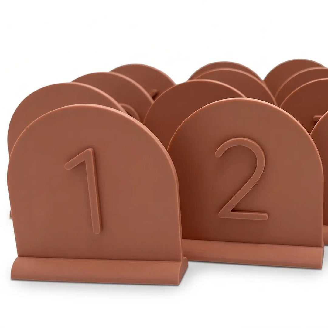 Número de mesa para boda en forma de arco color terracota con relieve sobre mesa de banquete decorada.