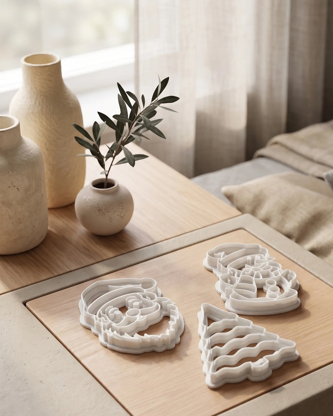 Set de tres cortadores de galletas blancos con forma de Papá Noel, árbol de Navidad y muñeco de nieve sobre una mesa de madera.